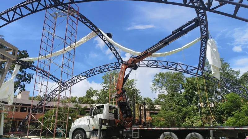 Grúa HIAB extendida junto a una membrana blanca sobre arcos metálicos y andamios rojos.