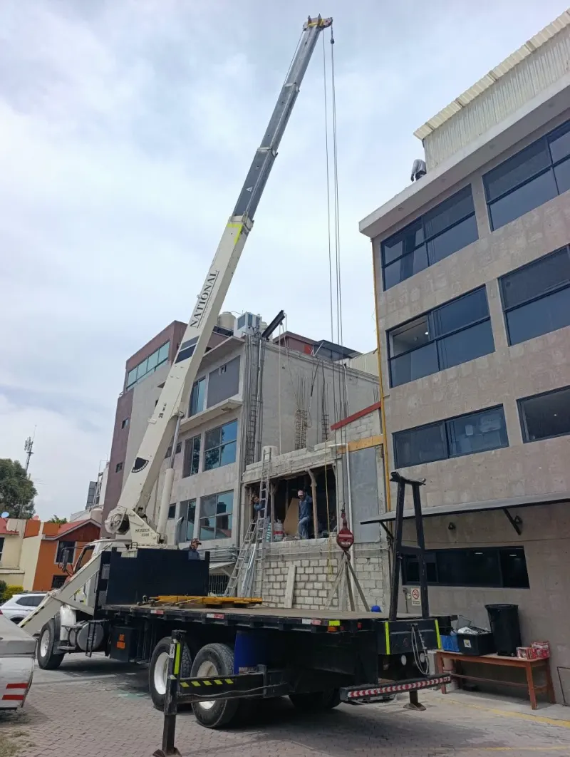 Aire acondicionado en caja suspendido con eslingas frente a la planta alta del edificio.
