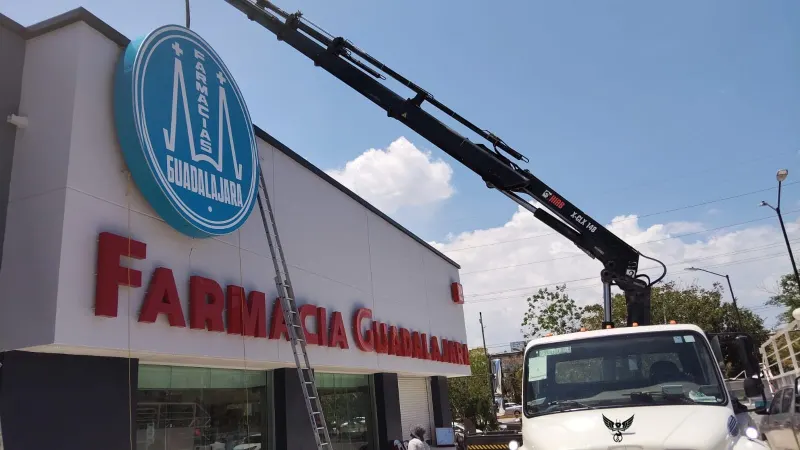 Pluma articulada sostiene un anuncio frente a una fachada mientras personal trabaja desde escaleras.