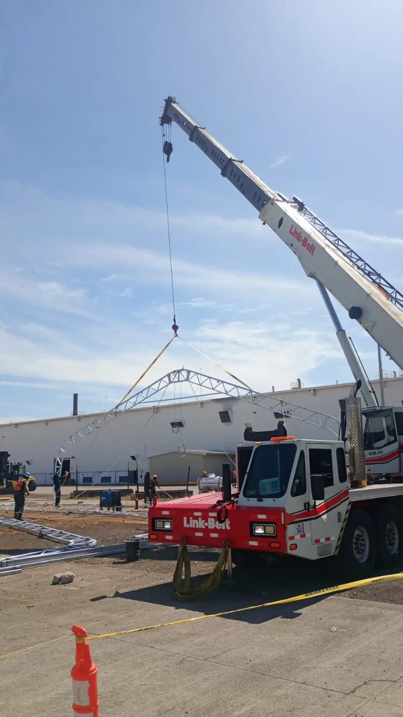 Grúa telescópica elevando un arco metálico sobre una estructura de arcos ya instalada.