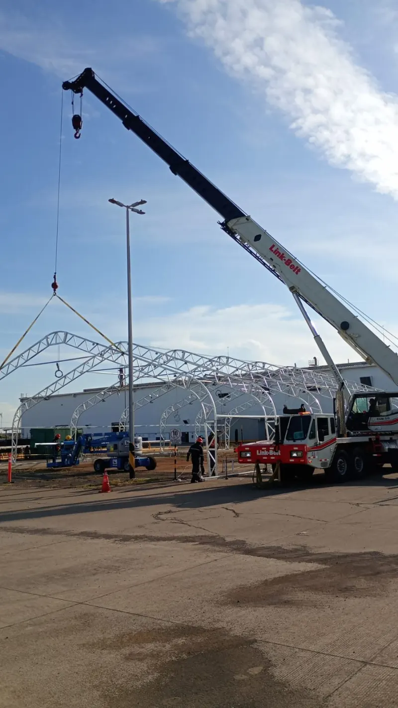 Conjunto de arcos metálicos unidos y sostenidos con cuerdas sobre una explanada industrial.