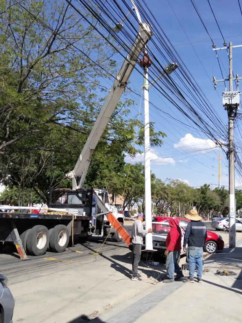 Grúa Titán junto a un poste de alumbrado vertical, con trabajadores y líneas aéreas alrededor.