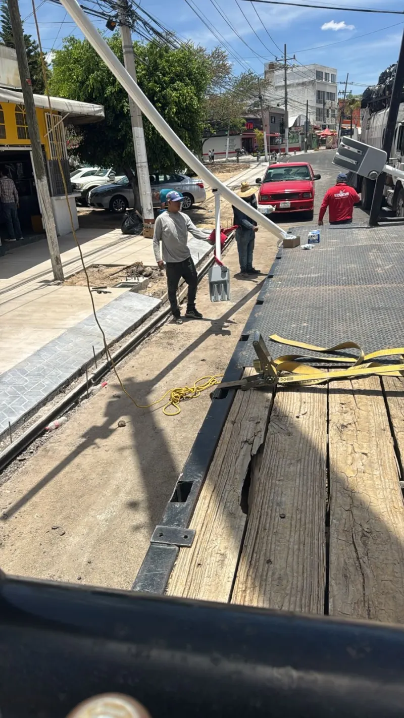 Poste blanco inclinado junto a la plataforma mientras trabajadores controlan su descenso.