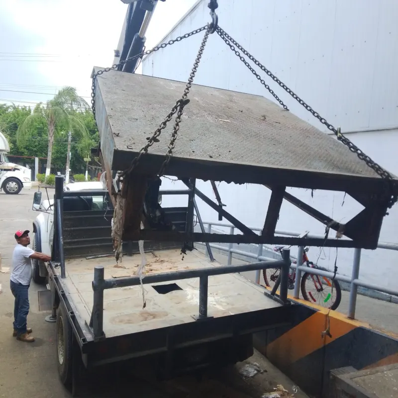 Rampa niveladora suspendida con cadenas sobre barandales y tarimas apiladas.